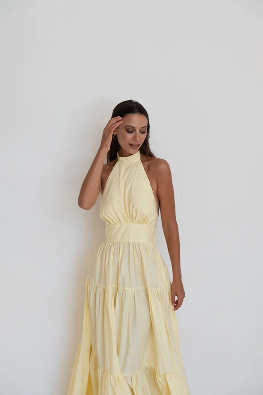 Model with hand up to face wearing Audrey Dress in Butter Yellow with halter neck - designer dress rental from Lend the Label