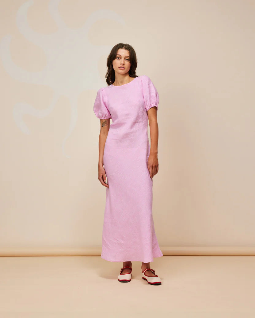 Model wearing KOS Linen Maxi Dress in soft pink with puff sleeves and a cut-out back on a neutral background.