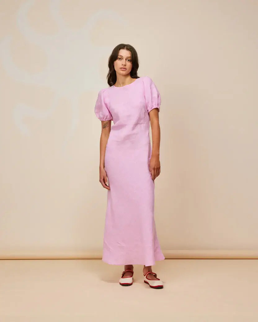 Model wearing KOS Linen Maxi Dress in soft pink with puff sleeves and a cut-out back on a neutral background.