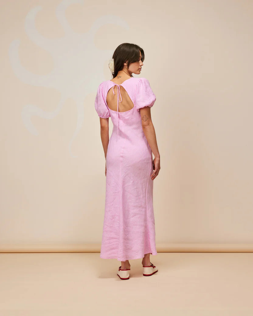 Model wearing KOS Linen Maxi Dress in soft pink with puff sleeves and a cut-out back, set against a minimalist background.
