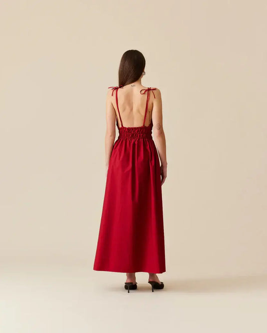 Model wearing and showcasing back of Ruby Hero Maxi Dress in Red. Made from luxurious garnet red cotton, it's perfect for any occasion.