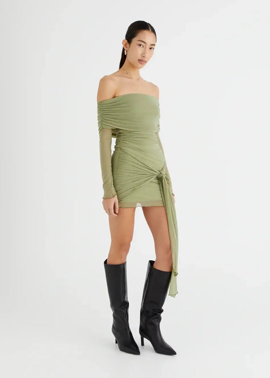 Model wearing Yasmin Off Shoulder Mini Dress in olive green, with sleek black boots and a sarong style skirt for a chic look.
