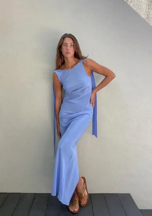 Model showcasing the Wilmer Dress in cornflower blue, featuring adjustable shoulder ties and high split hem, perfect for occasions.