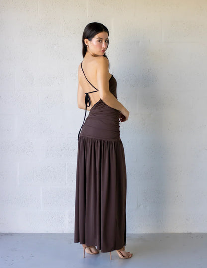 Lena Maxi Dress with asymmetrical style, gathered bodice, side cut-outs, and flowy skirt in brown color.