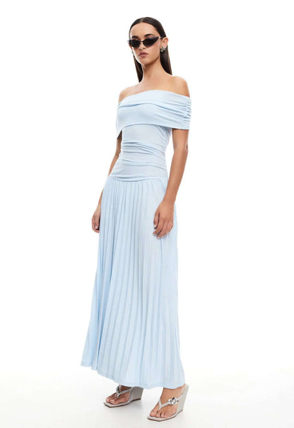 Model wearing Lioness Maxi dress in light blue, showcasing off-the-shoulder design and pleated skirt for effortless glamour.
