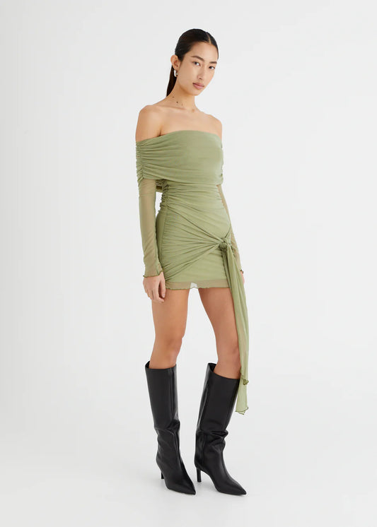 Model wearing Yasmin Off Shoulder Mini Dress in olive green, with sleek black boots and a sarong style skirt for a chic look.