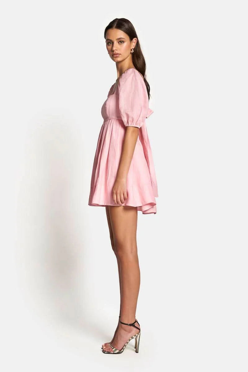 Aerin Open Back Tie Mini Dress in Baby Pink with puff sleeves and pleated skirt, showcasing side view.